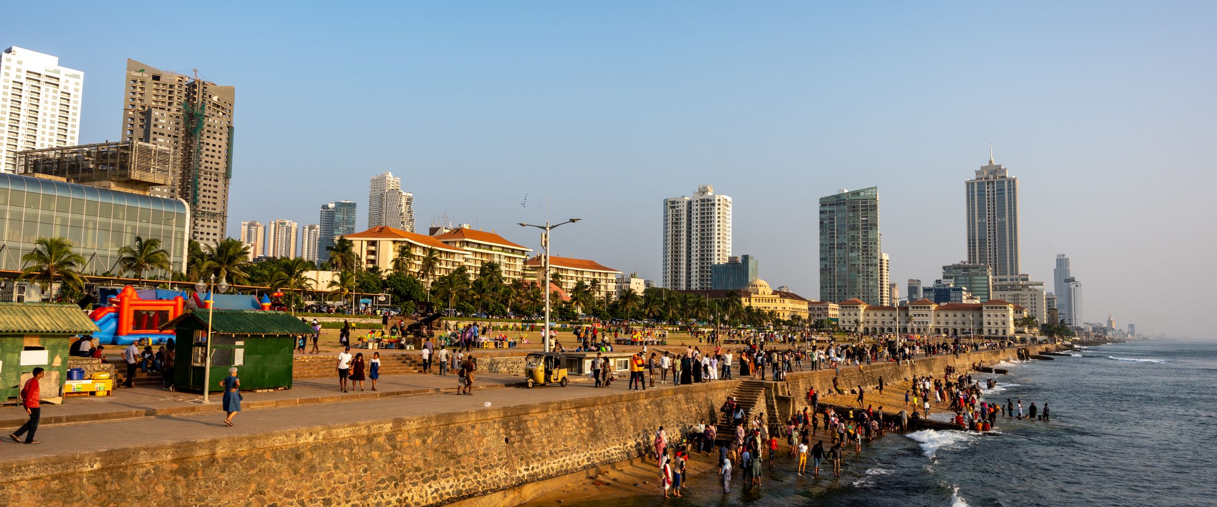 People walking along the seafront promenade in Colombo at golden hour, with the city skyline behind them.