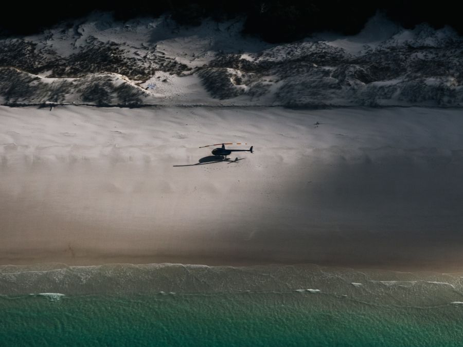 A helicopter in flight above a turquoise tropical coastline