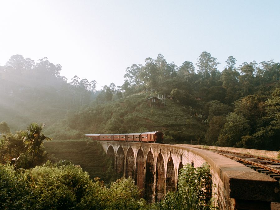 A train crossing the Nine Arch Bridge through dense green hillside near Ella