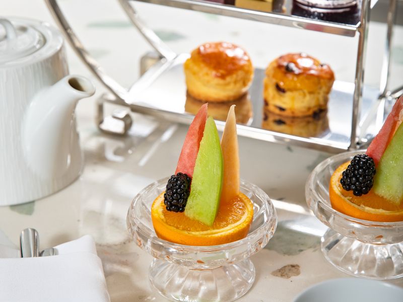 An afternoon tea stand laid with scones, pastries and fruit on a linen table.
