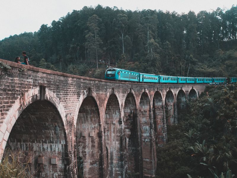 A blue train crossing the Nine Arch Bridge surrounded by jungle near Ella, Sri Lanka.